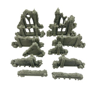 May include: A collection of gray miniature ruined structures, including archways, walls, and debris. The pieces are designed to resemble weathered stone, suitable for tabletop gaming or model building. The set includes various sizes and shapes.