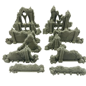 May include: A collection of gray miniature ruined structures, likely for tabletop gaming or model building. The pieces include sections of walls, arches, and architectural details, all with a weathered, damaged appearance. The set appears to be made of a durable material.