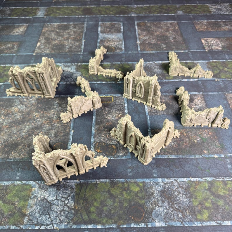 May include: A collection of eight beige, unpainted miniature building ruins featuring gothic-style arched windows and weathered stone textures. These small, modular terrain pieces are designed for tabletop gaming and display intricate architectural details.