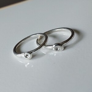 May include: Two silver rings with a small, circular design on the front. The rings are simple and delicate.