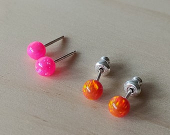 May include: A pair of stud earrings with a pink and orange opal stone. The earrings are silver and have a post back.