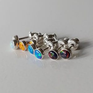 May include: A set of seven opal earrings in various colours, including white, orange, blue, black, and red. The earrings are silver and have a small post.