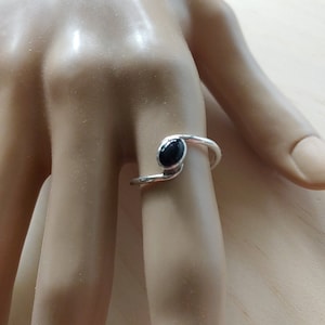 May include: A silver ring with a black oval gemstone. The ring is designed to be worn on the finger, with the stone facing upwards.