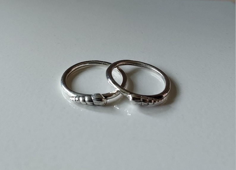 K&ouml;nnte beinhalten: Zwei silberne Ringe mit einem strukturierten Design. Die Ringe sind ineinander verschlungen.