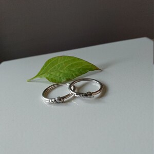 K&ouml;nnte beinhalten: Zwei silberne Ringe mit einem strukturierten Design. Die Ringe liegen auf einer wei&szlig;en Oberfl&auml;che mit einem gr&uuml;nen Blatt.