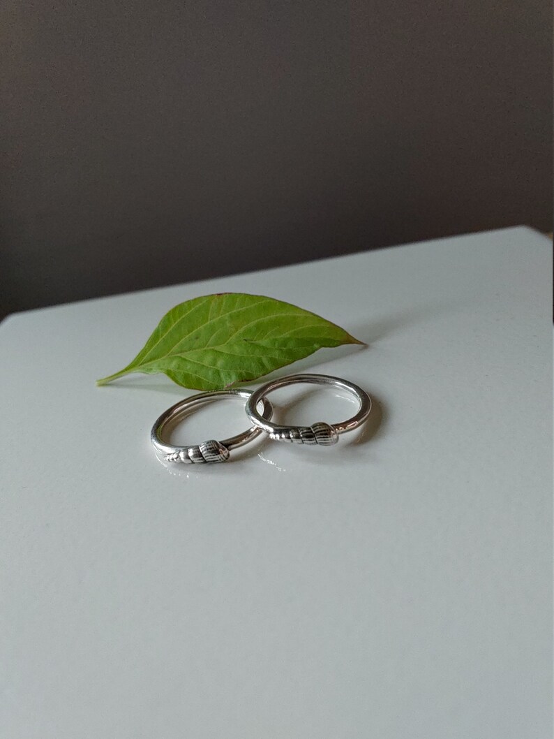K&ouml;nnte beinhalten: Zwei silberne Ringe mit einem strukturierten Design. Die Ringe liegen auf einer wei&szlig;en Oberfl&auml;che mit einem gr&uuml;nen Blatt.
