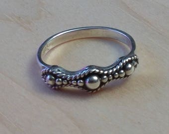 Puede incluir: Un anillo de plata con un diseño ondulado y pequeñas cuentas. El anillo tiene tres cuentas más grandes en el centro.