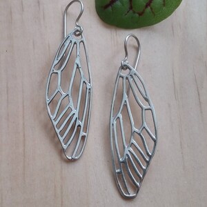 May include: A pair of silver earrings with a delicate butterfly wing design. The earrings are made of metal and have a dangling style.