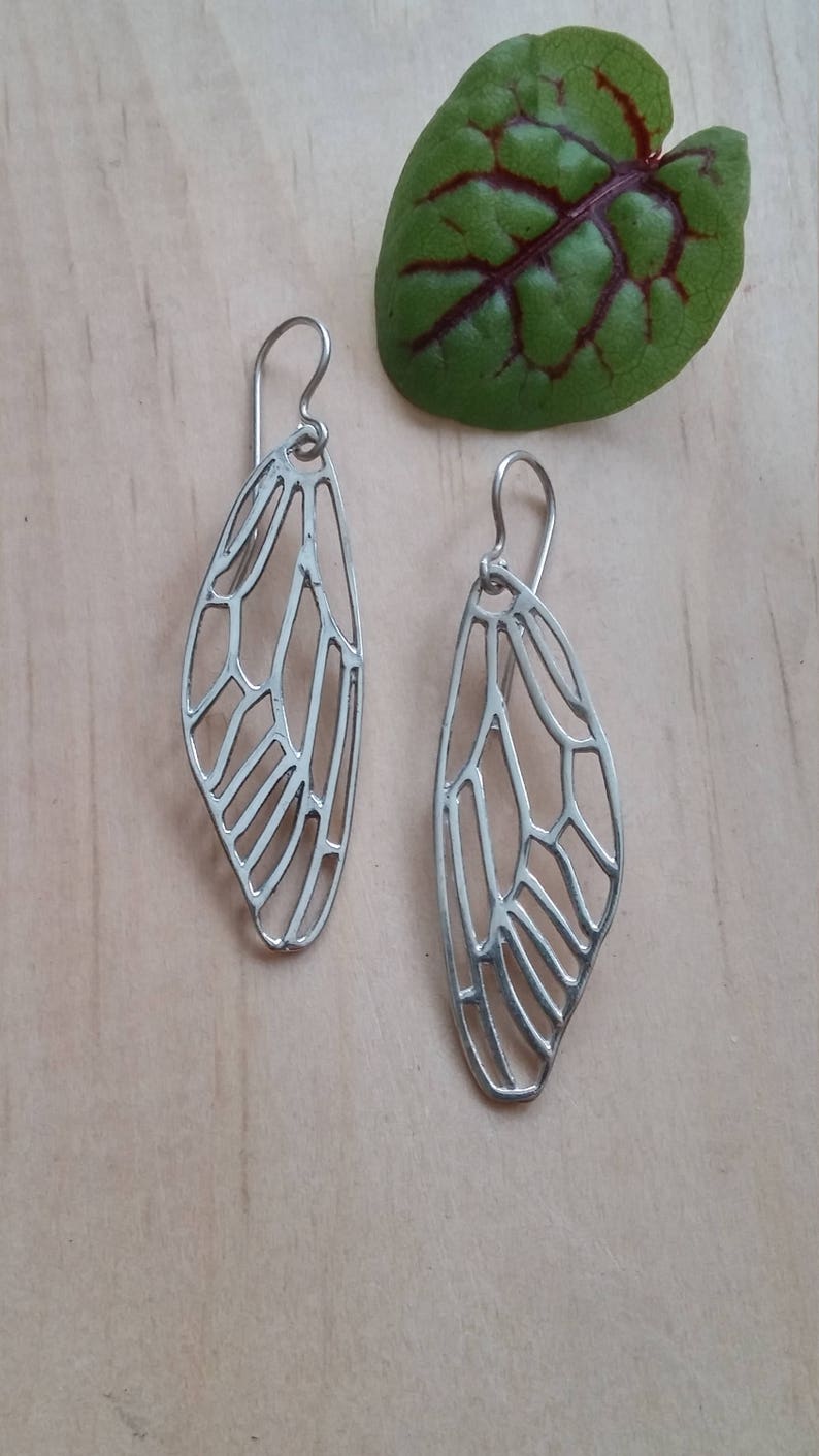 May include: A pair of silver earrings with a delicate butterfly wing design. The earrings are made of metal and have a dangling style.