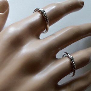 K&ouml;nnte beinhalten: Zwei silberne Ringe mit einem strukturierten Design. Die Ringe werden an einer Mannequin-Hand getragen.