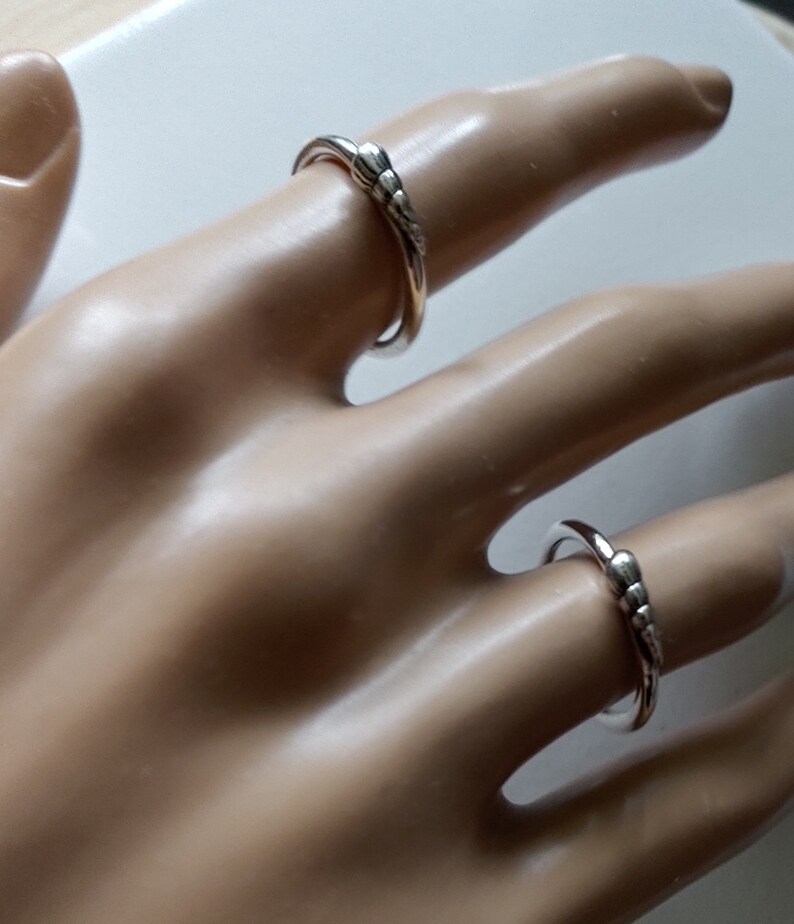 K&ouml;nnte beinhalten: Zwei silberne Ringe mit einem strukturierten Design. Die Ringe werden an einer Mannequin-Hand getragen.