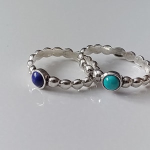 May include: Two silver rings with beaded bands and small gemstone settings. One ring has a blue gemstone and the other has a turquoise gemstone.