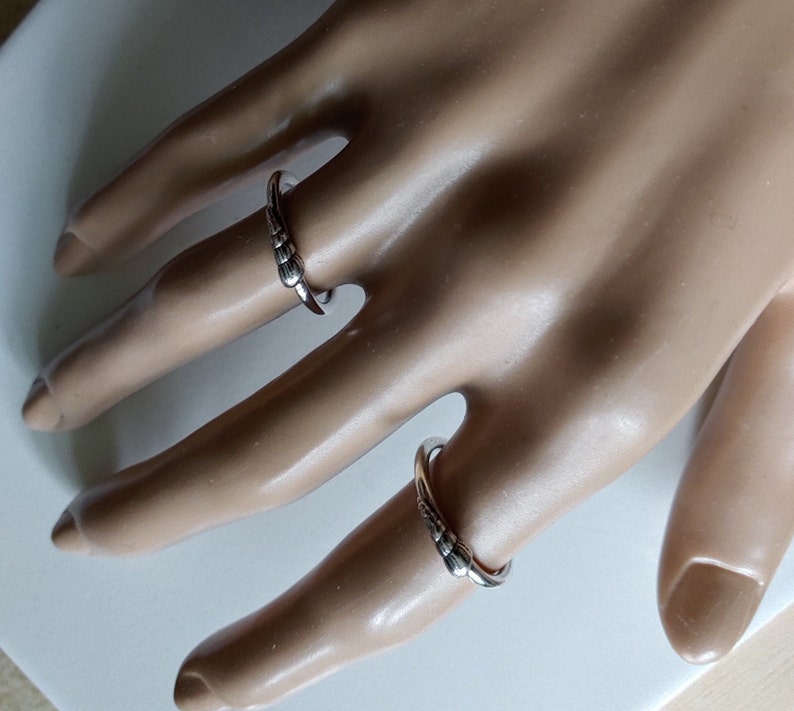 K&ouml;nnte beinhalten: Zwei silberne Ringe mit einem strukturierten Design. Die Ringe werden an den Fingern einer Mannequin-Hand getragen.