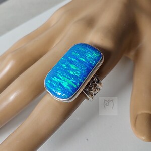 May include: A silver ring featuring a large, rectangular blue opal gemstone. The opal displays a green and blue iridescent sheen.