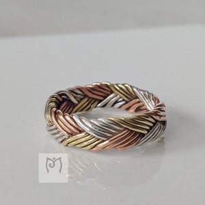 May include: A braided ring made of silver, copper and brass. The ring is woven in a complex pattern and has a smooth, polished finish.