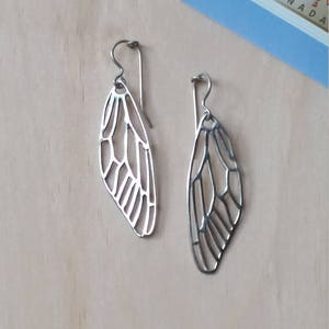 May include: A pair of silver butterfly wing earrings. The earrings are made of a delicate, openwork design and hang from silver hooks.