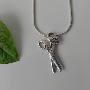May include: A silver chain necklace with a silver scissor charm.