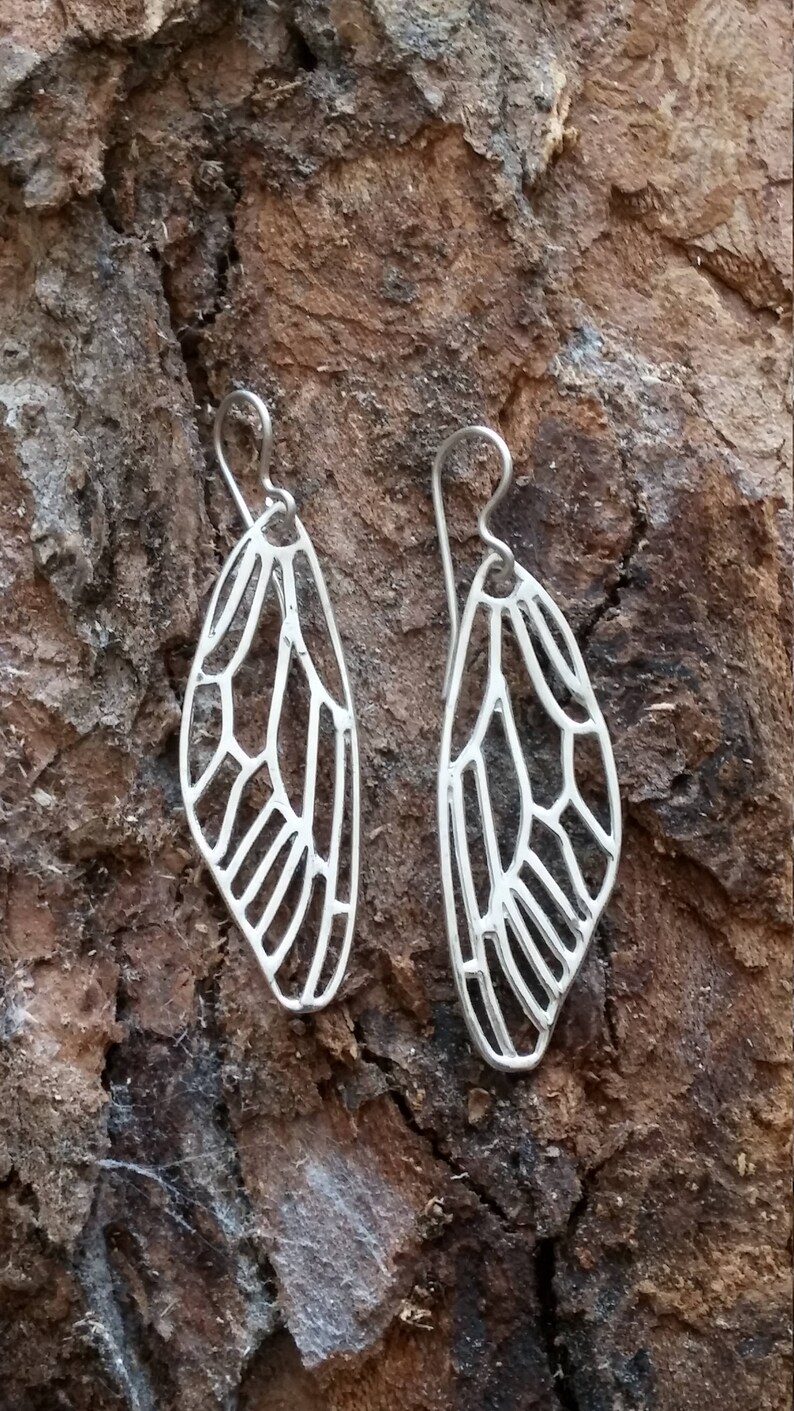 May include: A pair of silver earrings shaped like dragonfly wings. The wings are delicate and intricate, with a detailed vein pattern.