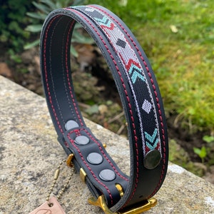 May include: Black leather dog collar with red stitching and a geometric pattern in turquoise, gray, and red. The collar has a brass buckle and a tag that says "Coco".