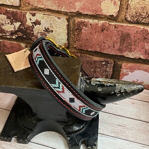 May include: Black leather dog collar with a red, white, and blue geometric pattern. The collar is on a black metal anvil.