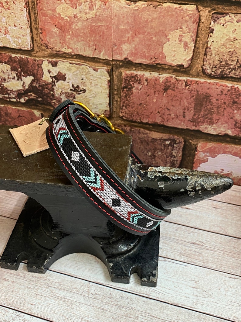 May include: Black leather dog collar with a red, white, and blue geometric pattern. The collar is on a black metal anvil.