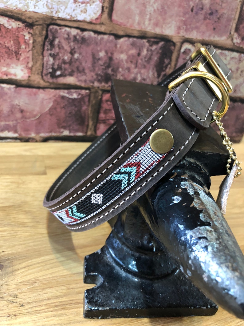 May include: A brown leather dog collar with a geometric patterned fabric insert. The collar has a brass buckle and D-ring.