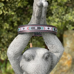 May include: Black leather dog collar with a red stitched edge and a colorful geometric pattern of white, red, blue, and green beads.