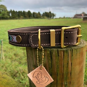 May include: Brown leather dog collar with a brass buckle and a decorative woven strip. The collar is attached to a wooden post with a leather tag that says "B&B".