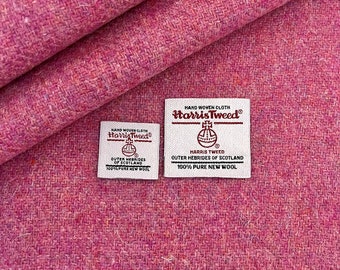 Peut inclure: Gros plan sur un tissu Harris Tweed rose avec deux étiquettes blanches. Les étiquettes indiquent "HAND WOVEN CLOTH Harris Tweed®" et comprennent le logo Harris Tweed Orb. Le texte sur les étiquettes indique "HARRIS TWEED OUTER HEBRIDES OF SCOTLAND 100% PURE NEW WOOL".
