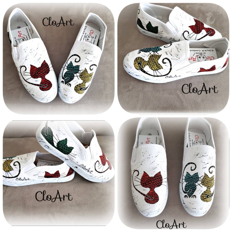 May include: A pair of white canvas slip-on shoes with a hand-painted design of two cats. The cats are painted in red, green, and yellow. The shoes have a white background with black splatter paint. The shoes are labeled "CloArt".