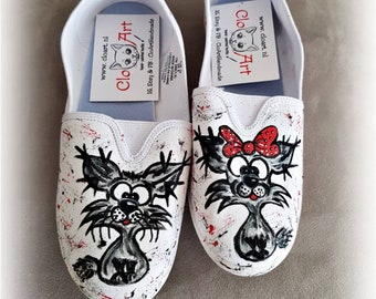 Könnte beinhalten: Ein Paar weiße Leinenschuhe mit handgemalten Comic-Katzen. Eine Katze trägt eine rote Schleife. Die Schuhe haben rote und schwarze Farbspritzer.