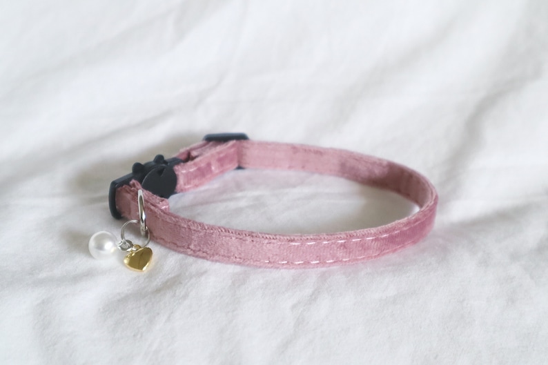 May include: A pink velvet cat collar with a silver bell and a gold heart charm.