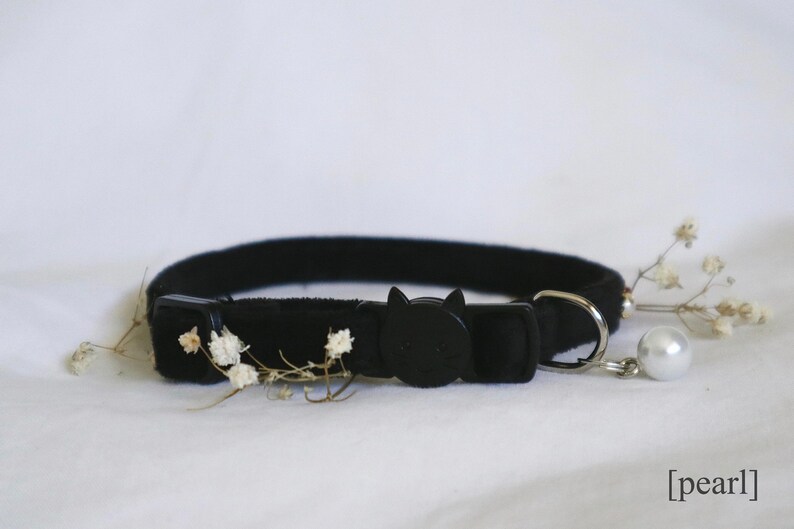 May include: Black cat-shaped breakaway collar with a white pearl charm. The collar is made of soft velvet and has a safety buckle.