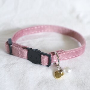 May include: A pink velvet cat collar with a black cat-shaped buckle and a gold heart charm with a white pearl.
