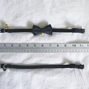 May include: A black cat collar with a black bow tie and a bell. The collar is adjustable and has a safety buckle. The collar is measured against a ruler with markings from 1 to 14.