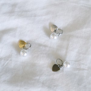 May include: Three pairs of heart-shaped earrings with pearl accents. The earrings are silver, gold, and black.