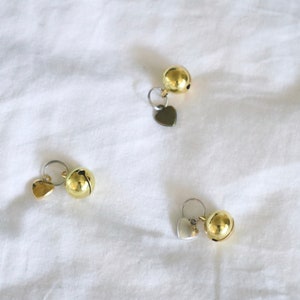 May include: Three gold-colored bells with heart-shaped charms. The bells are attached to silver rings.