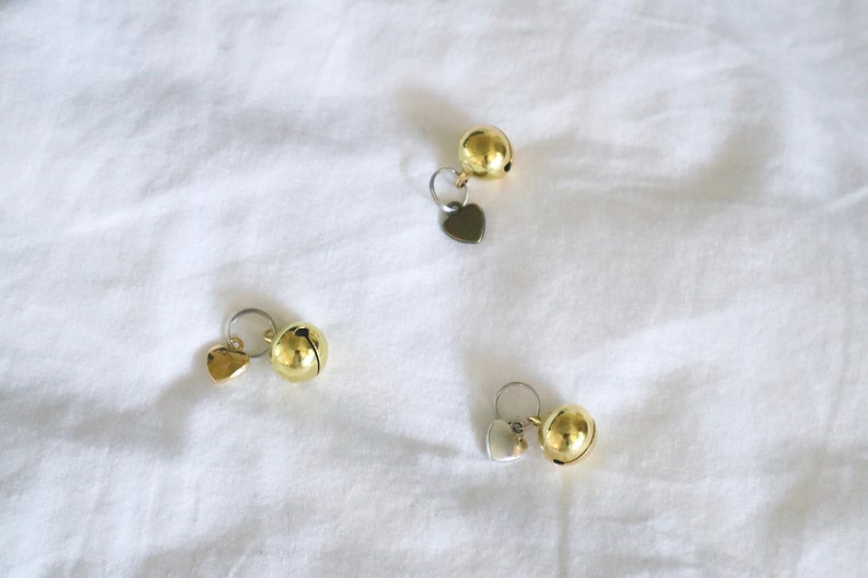 May include: Three gold-colored bells with heart-shaped charms. The bells are attached to silver rings.