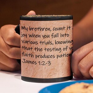 Puede incluir: Taza de café negra con fondo beige y texto blanco que dice "Mis hermanos, considérenlo un gozo cuando caigan en diversas pruebas, sabiendo que la prueba de su fe produce paciencia. Santiago 1:2-3"
