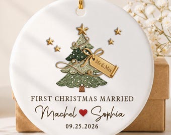 May include: A round white ceramic ornament featuring a green Christmas tree illustration with a gold star topper, a gold gift tag labeled Mr & Mrs, and the text FIRST CHRISTMAS MARRIED, Machel, a red heart, Sophia, and 09.25.2026.