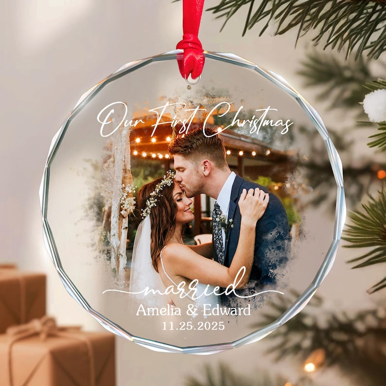 May include: A clear, faceted glass Christmas ornament with a red ribbon. The ornament features a photo of a couple and the text "Our First Christmas", "married", the names "Amelia & Edward", and the date "11.25.2025".