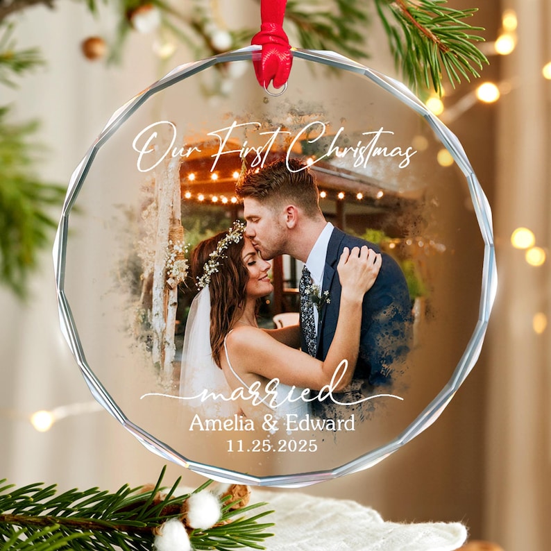 May include: A clear, faceted glass Christmas ornament with a red ribbon. The ornament features a photo of a couple kissing, with the words "Our First Christmas" and "married" in script. The names "Amelia & Edward" and the date "11.25.2025" are also included.