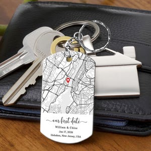 May include: A silver keychain with a map design and the text "our first date." The keychain includes the names William & Chloe, the date January 17, 2026, and Hoboken, New Jersey, USA. Keys and a house-shaped keychain are also visible.