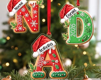 May include: Three letter-shaped Christmas ornaments shaped like gingerbread cookies. The letters N, D, and A are decorated with red or green icing, white snowflakes, holly leaves, and a Santa hat. Each features a name and the year 2026.