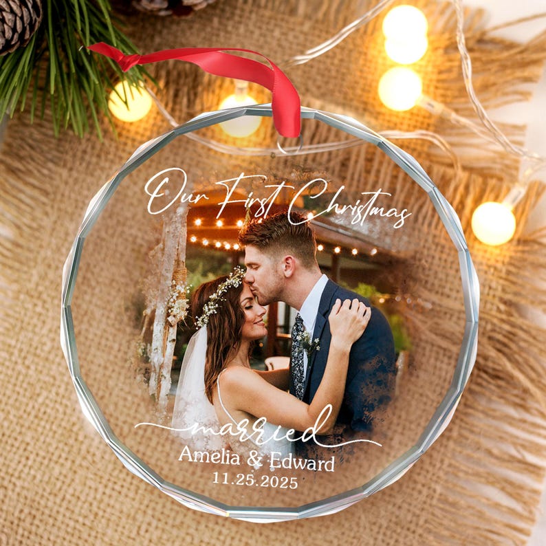 May include: A clear, round Christmas ornament with a photo of a couple kissing. The ornament has the words "Our First Christmas" and "married" written on it, along with the names "Amelia & Edward" and the date "11.25.2025". A red ribbon is attached.
