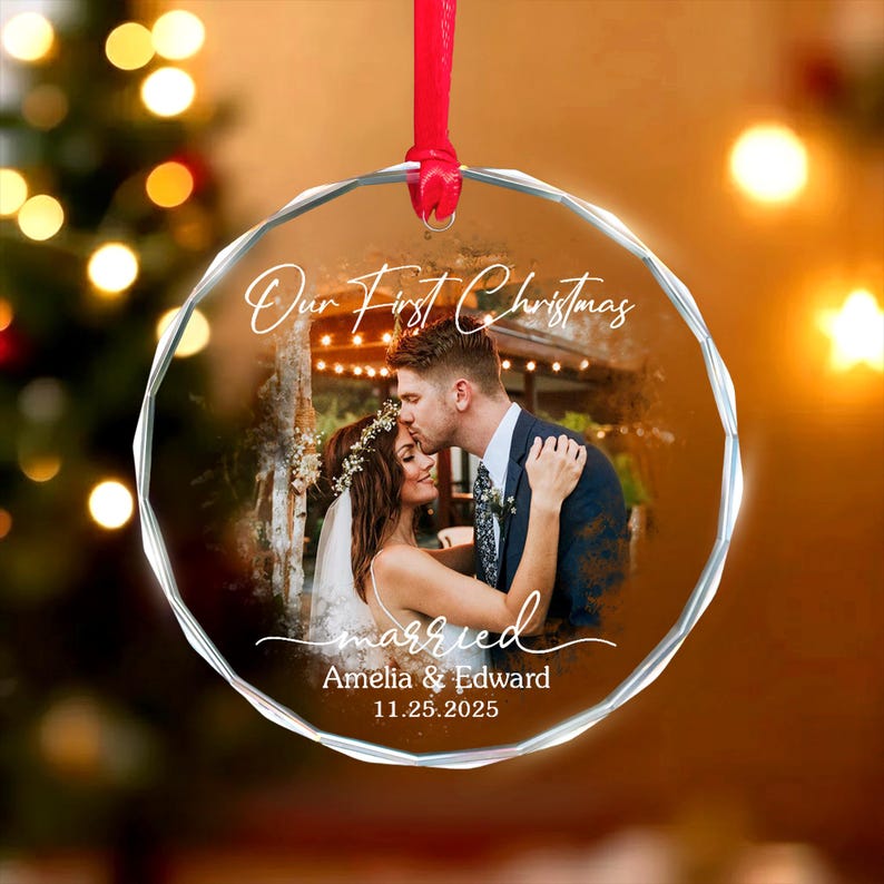 May include: A clear, faceted glass Christmas ornament with a photo of a couple kissing. The ornament has the text "Our First Christmas" and "married" in script, along with the names "Amelia & Edward" and the date "11.25.2025". A red ribbon is attached for hanging.