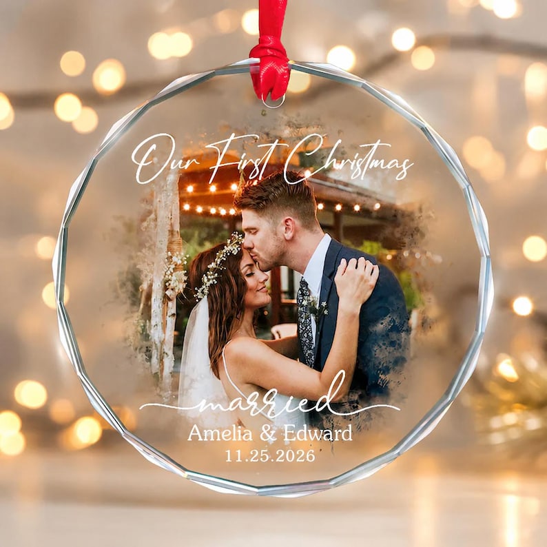 May include: A clear, faceted glass Christmas ornament with a red ribbon. The ornament features a photo of a couple kissing, with the words "Our First Christmas" and "married" in script. The names "Amelia & Edward" and the date "11.25.2025" are also included.
