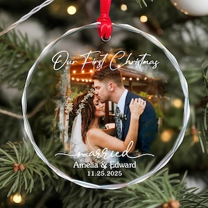 May include: A clear, round Christmas ornament with a photo of a couple kissing. The ornament has the text "Our First Christmas" and "married" with the names Amelia & Edward and the date 11.25.2025. A red ribbon is attached for hanging.