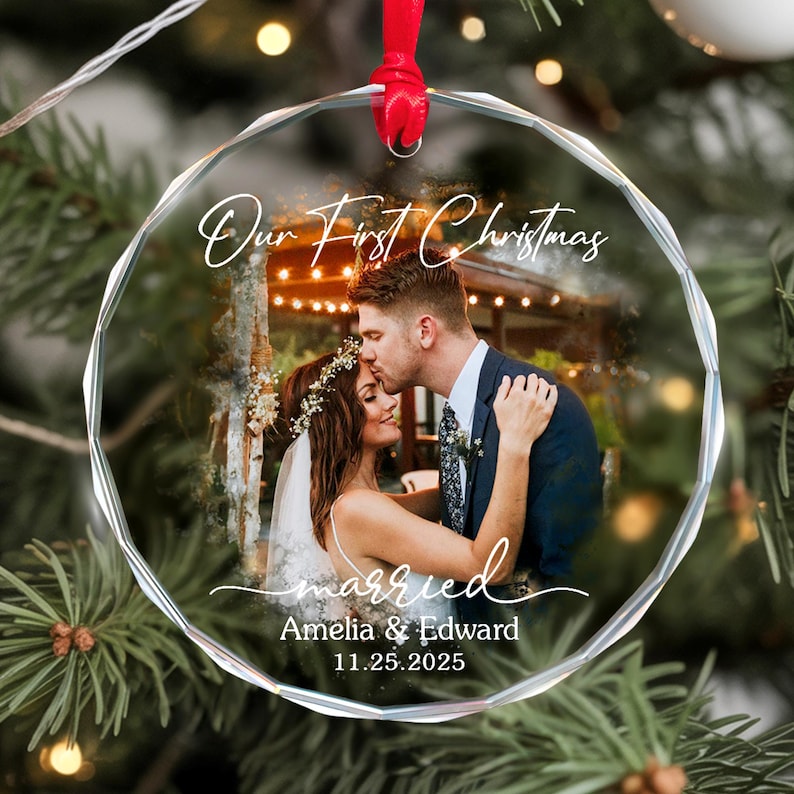 May include: A clear, round Christmas ornament with a photo of a couple kissing. The ornament has the text "Our First Christmas" and "married" with the names Amelia & Edward and the date 11.25.2025. A red ribbon is attached for hanging.