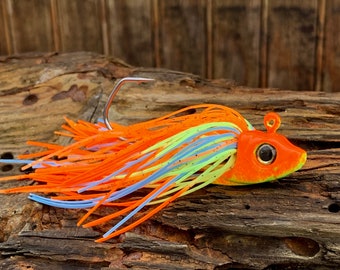 Könnte beinhalten: Orangefarbener, blauer und grüner Angelköder mit einem Einzelhaken. Der Köder hat eine realistische Fischform mit einem großen Auge.
